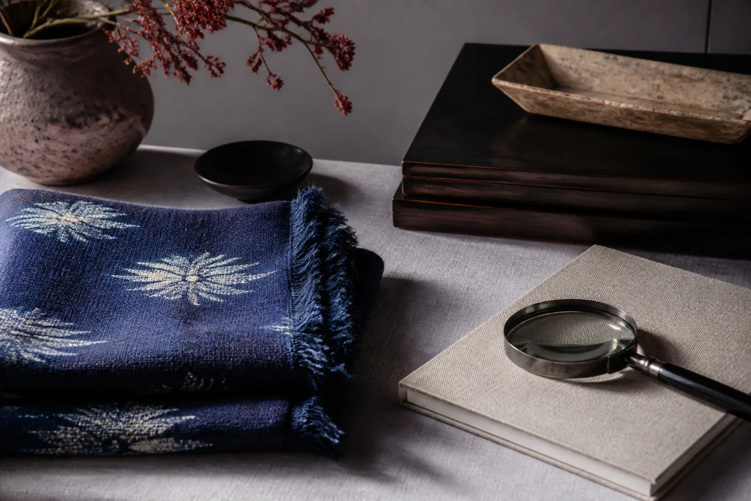 Folded indigo textile, magnifying glass and blank notebook on an editorial desk