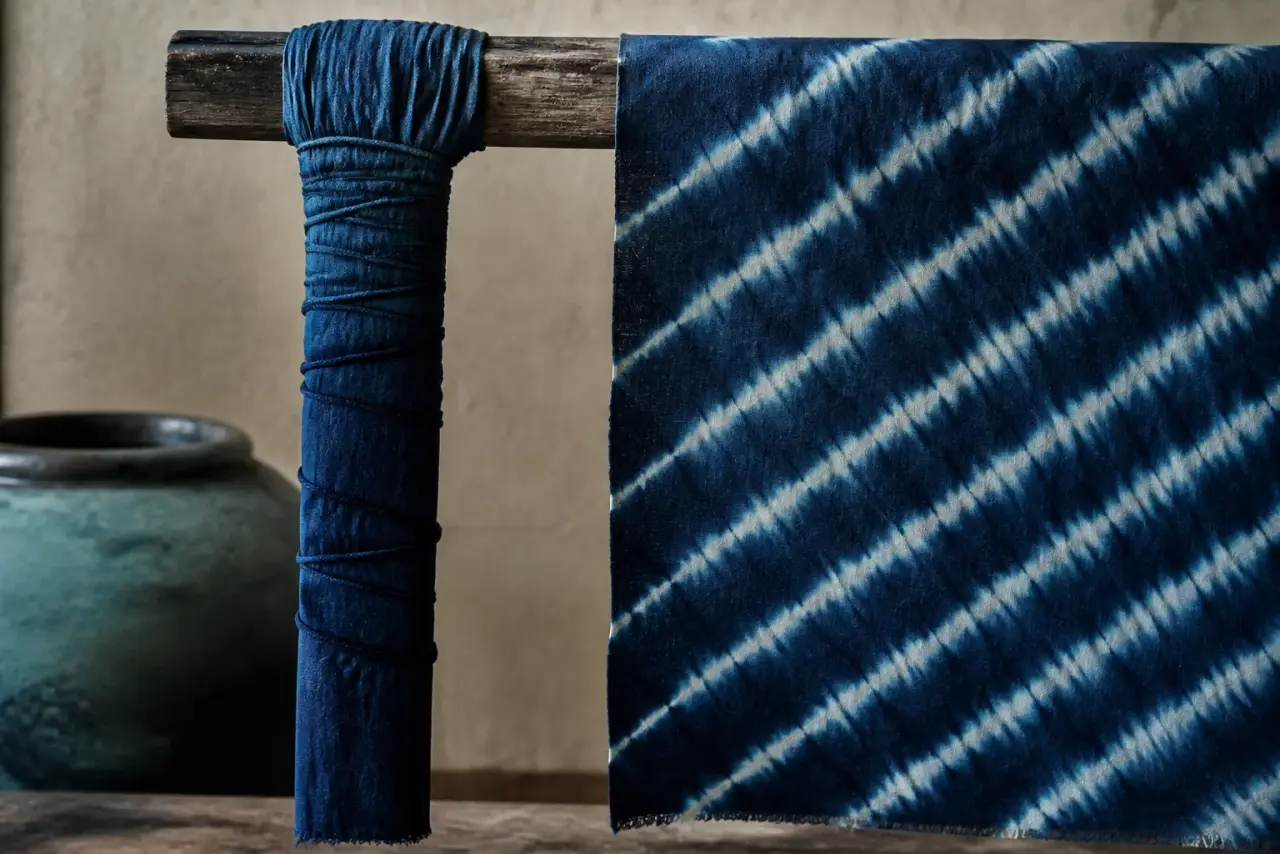 Pole-wrapped cloth beside an opened indigo textile with diagonal pleats