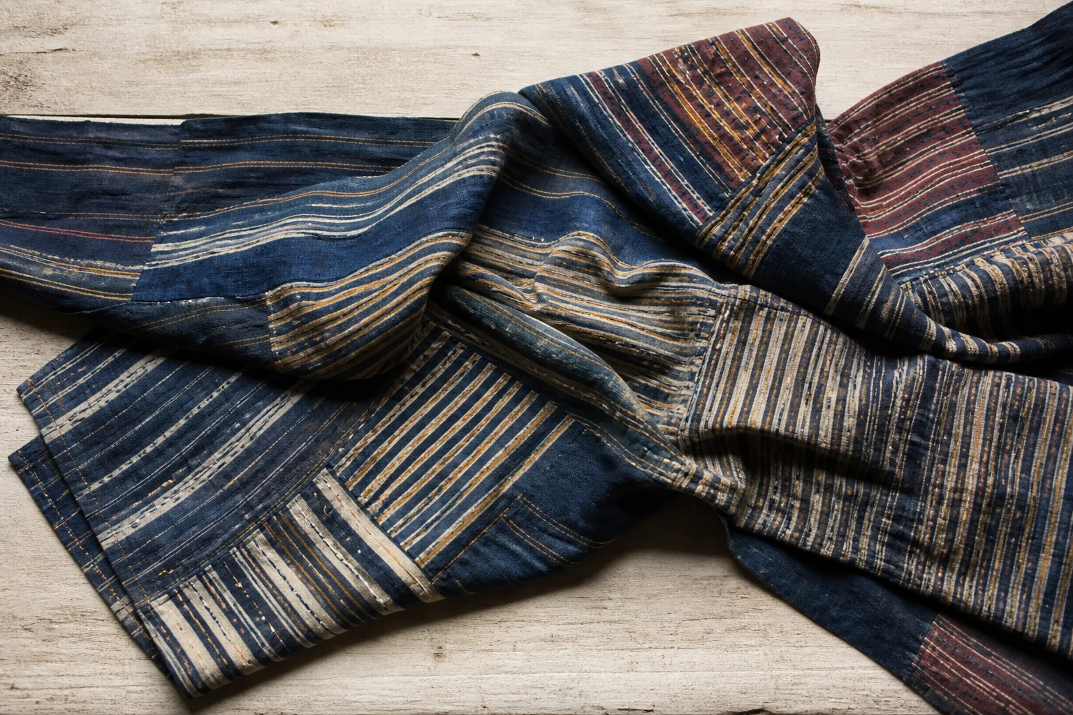 A folded length of heavy worsted tartan cloth on a wooden mill table, its warp threads catching low window light.